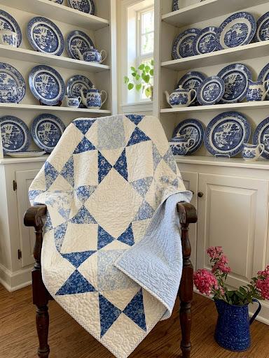 The Something Blue quilt draped over a wooden chair in a room of blue-and-white china