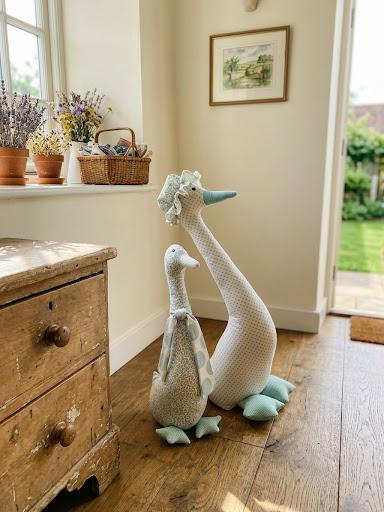 Two handmade fabric geese standing on a wooden floor beside an old pine chest
